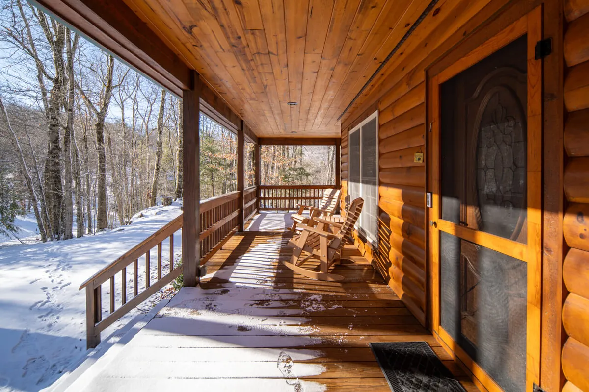 A close-up of a porch with wooden rocking chairs, snow resting on the porch and logs of the house. It highlights a calm, reflective atmosphere, ideal for enjoying coffee or taking breaks in nature.