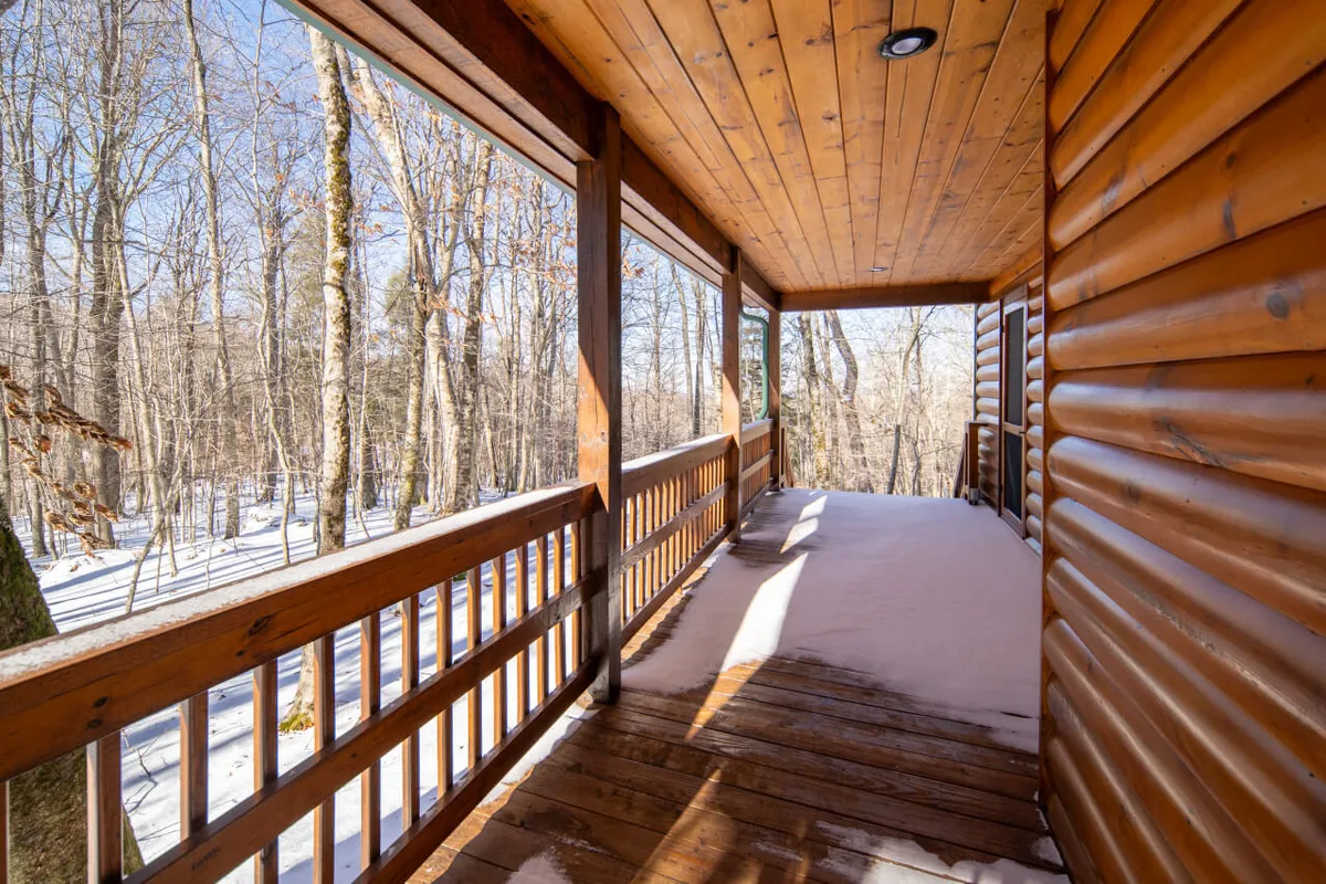 A peaceful wooden deck overlooks snow-dusted trees and expansive nature, with the porch surrounded by natural beauty. Although there’s a hint of winter, the deck’s design and open view illustrate the type of outdoor spaces guests can enjoy for stargazing, morning coffee, or relaxing after hiking and biking.