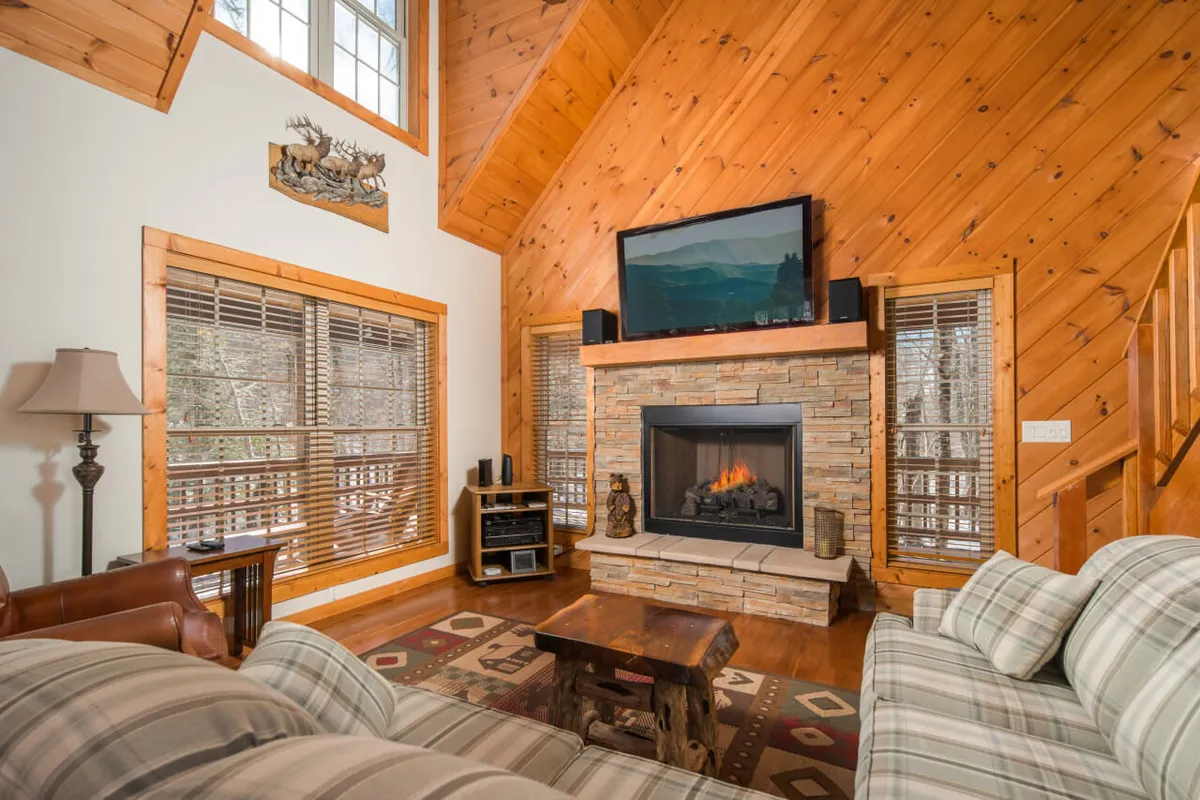 This image features a warm living area with a fireplace, large window, and comfortable sofa. The decorative wall art complements the inviting atmosphere and the window hints at the surrounding mountain views that are highlighted in the section.