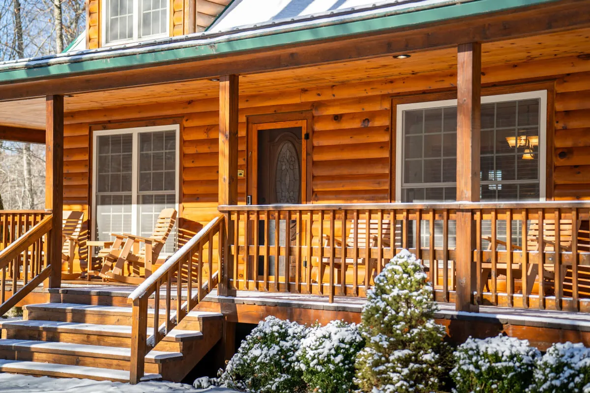 A welcoming wooden porch with comfortable rocking chairs and a view out onto the surrounding landscape. The scene exudes warmth and relaxation, suggesting a perfect spot to unwind after outdoor activities. The porch directly connects the interior living spaces to the natural beauty outside, emphasizing the lodge’s integration with its mountain surroundings.